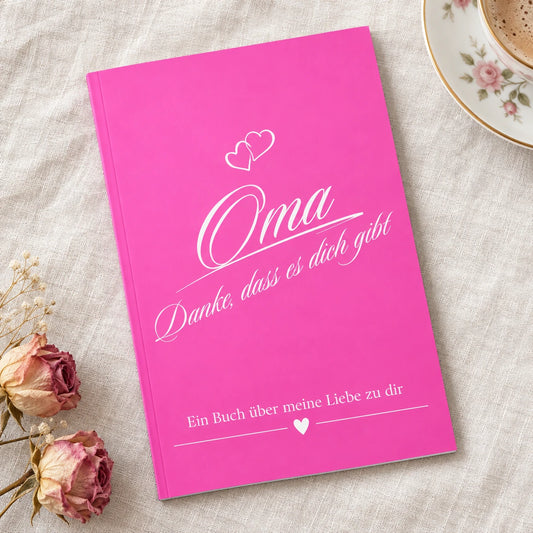Buch Oma – Danke, dass es dich gibt, pinker Einband, auf einer Leinendecke neben Tasse und Rosen